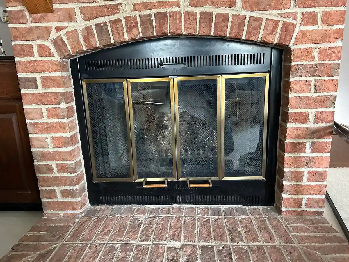 A red-brick masonry fireplace with a dated brass-framed door