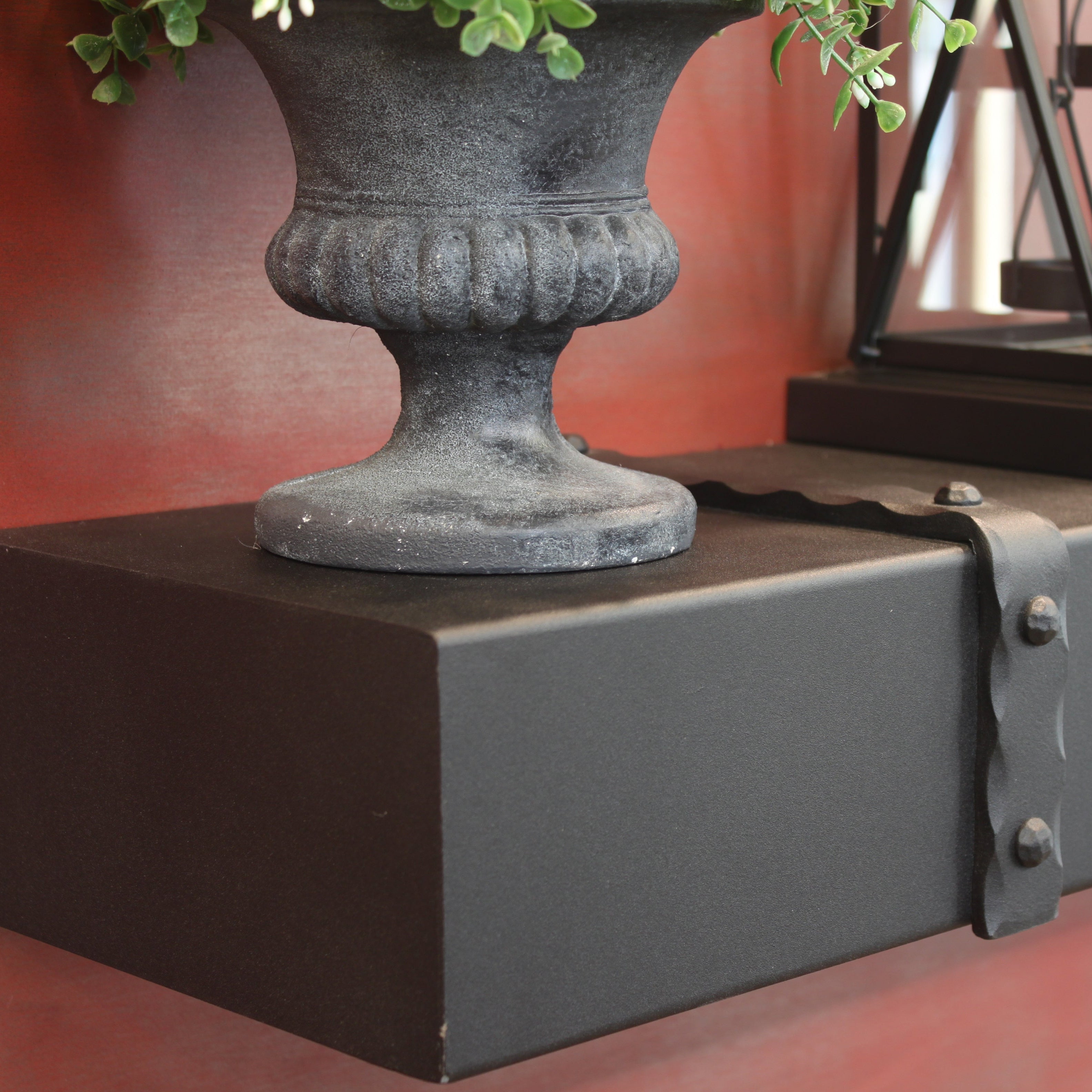 Decorative urn with greenery on a black pedestal against a red background