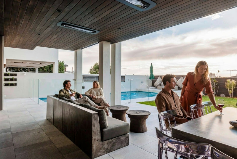 Bromic Tungsten Electric heaters recessed into a wood ceiling above a poolside outdoor dining and seating area. Manufacturer installation inspiration; accessories shown sold separately.