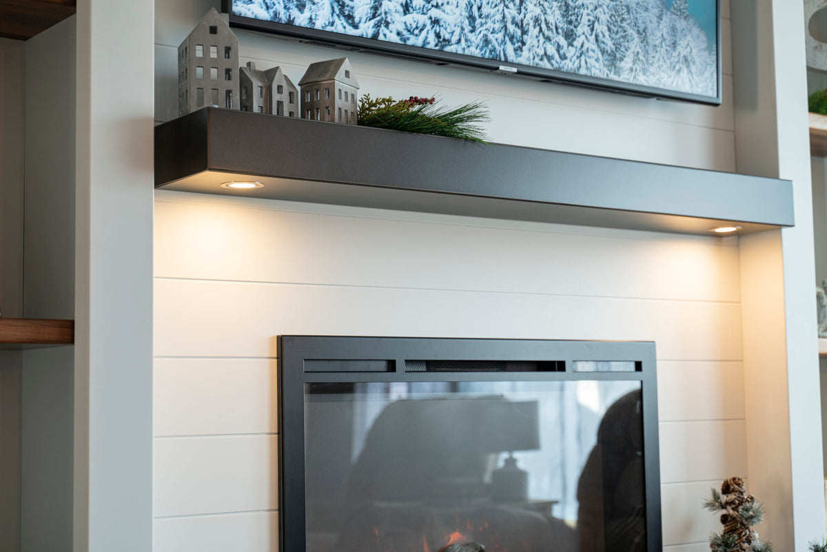 Metal mantel shelf with two downward-facing lights above a fireplace on a white wall